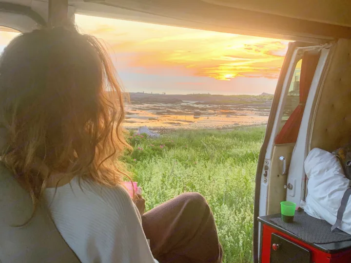 Stunning sunset over a rocky coast, viewed from an RV rental. A person relaxes inside, enjoying the serene view and peaceful road trip.. Chevrolet G20 1983