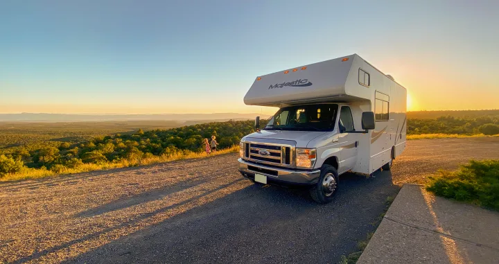 White Majestic RV rental parked on a hill overlooking a vast, forested valley at sunset. Two children are visible playing.. Thor Motor Coach Four Winds Majestic 2015