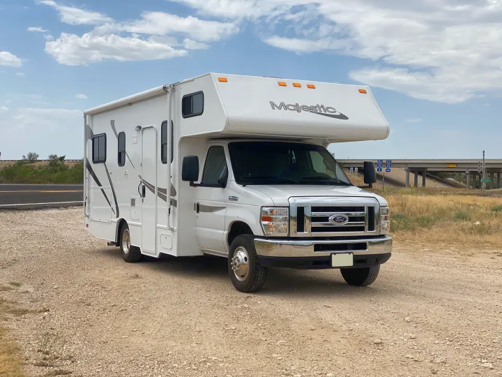 White Class C RV rental parked on a gravel shoulder. Blue sky, bridge in distance. Perfect for travel adventures.. Thor Motor Coach Four Winds Majestic 2015