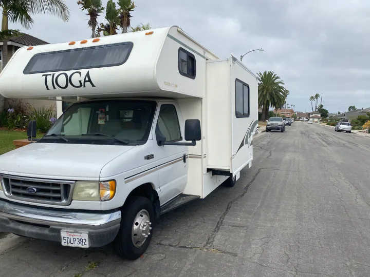 This white Tioga Class C RV, possibly an **rv rental**, is parked on a California residential street with its slide-out extended.. Fleetwood Tioga 2003