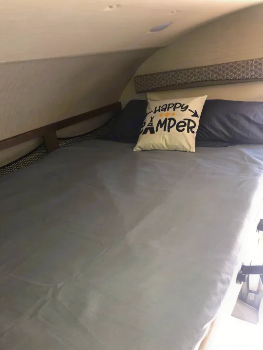 This RV rental features a cozy bunk bed with grey bedding, a 'happy camper' pillow, and a safety net, perfect for camping trips.. Jayco Greyhawk 2019