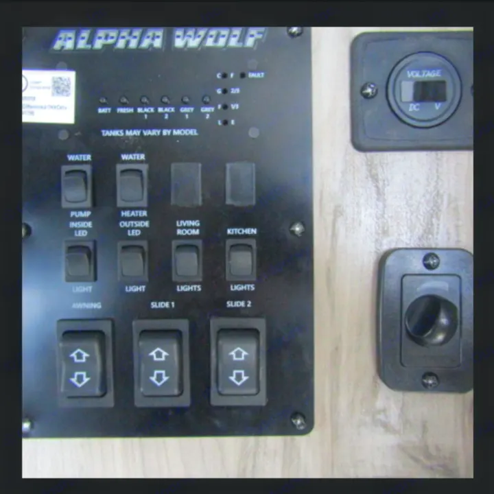 Inside an RV rental: a control panel displaying tank levels, battery voltage, and switches for lights, pumps, and slide-outs.. Forest River Cherokee Alpha Wolf 2021