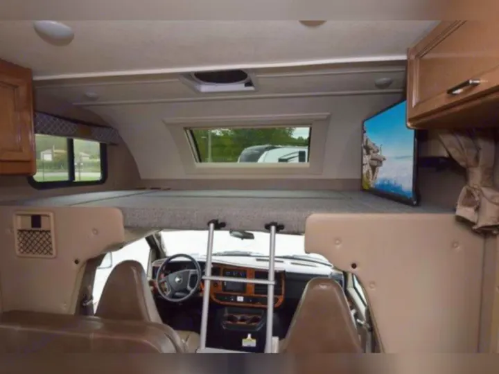Inside an RV rental: Looking towards the driver's cabin from the main living area, featuring an overhead bunk and mounted TV.. Thor Quantum 2020