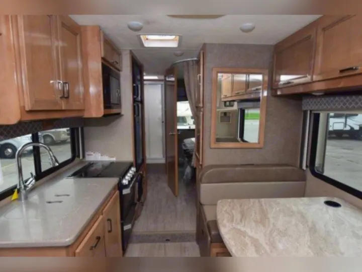 Inside this modern rv rental: a compact kitchen with sink, stove, and microwave, opposite a comfortable dinette area.. Thor Quantum 2020