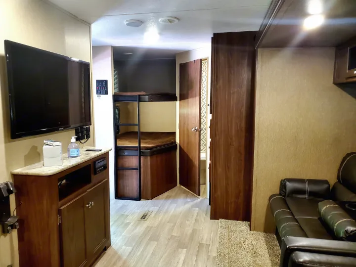 This RV rental interior features a cozy living area with TV, bunk beds, and a glimpse of the bathroom, ideal for family trips.. Coleman 285bh 2017