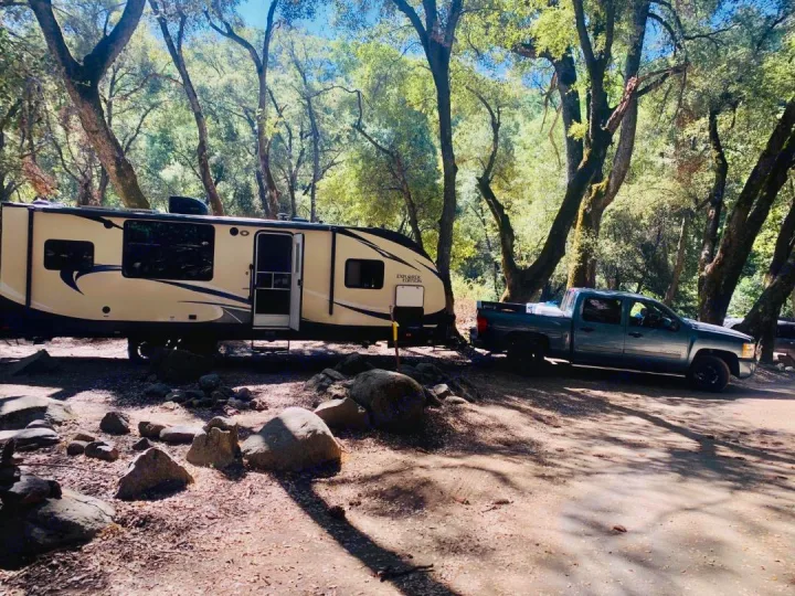 An RV rental travel trailer and a pickup truck are parked at a sunny, wooded campsite.. Forest River Evo 2017