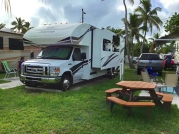 A white Jayco RV rental is parked on a grassy site at a tropical campground.. Jayco Redhawk 2020