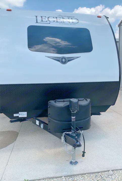 Front view of a white RV travel trailer, showcasing its covered propane tanks and hitch setup. Great for rv rental.. ForestRiver Surveyor 2020