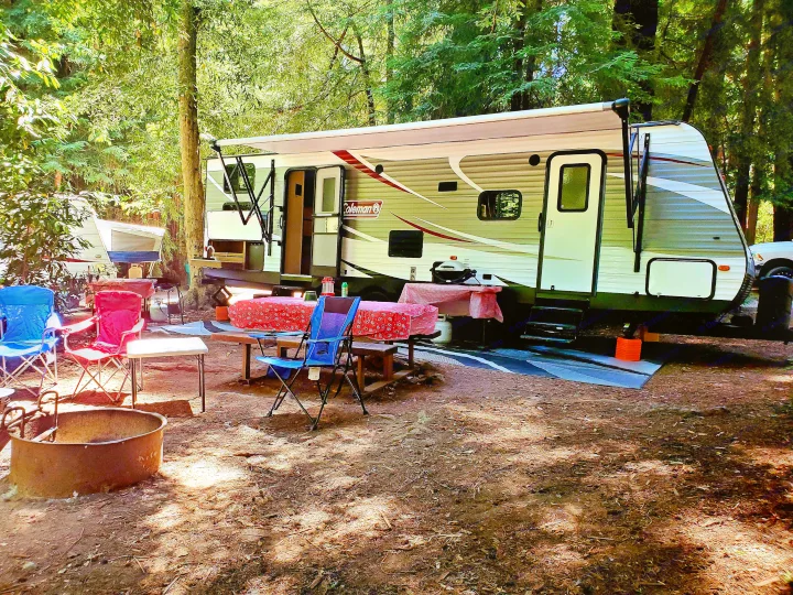 Serene forest campsite with an RV rental (Coleman travel trailer), ready for relaxation with chairs, tables, and a fire pit.. Coleman 285bh 2017