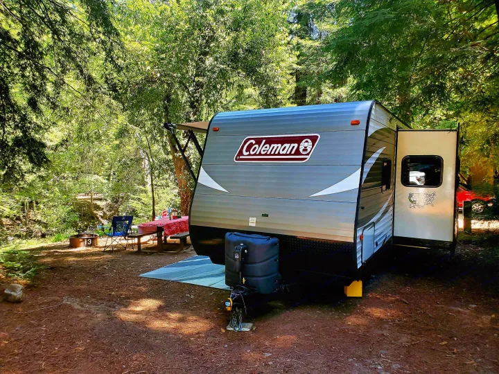 This RV rental is perfectly set up at a peaceful forest campsite, complete with a picnic table and fire pit, ideal for outdoor camping.. Coleman 285bh 2017