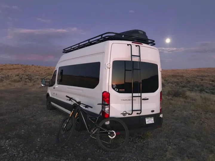 Adventure-ready RV rental: white camper van with bike, roof rack, under a full moon.. Ford Transit Custom 2015