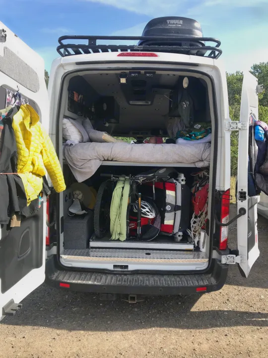 RV rental van with open back, showing packed interior: bikes, gear, and bedding. Thule cargo box on roof.. Ford Transit Custom 2015
