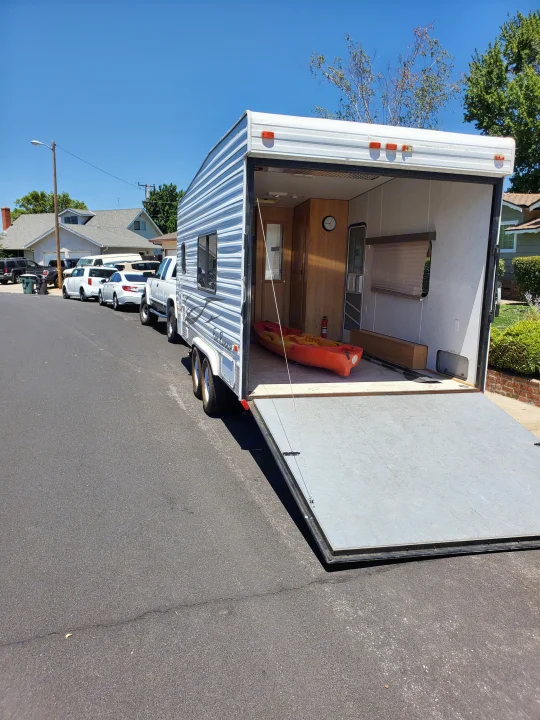 RV rental toy hauler parked on a street, with its rear ramp down revealing an orange kayak & paddles inside. Sunny day.. Carson Trailer Toy Hauler 2007
