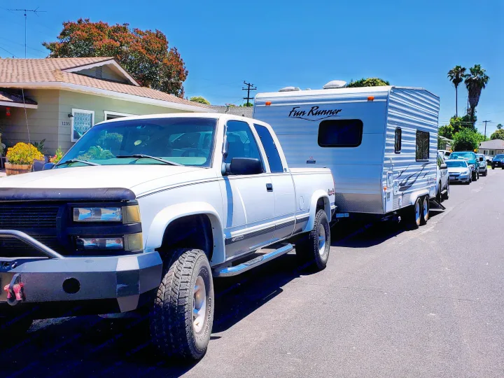 White pickup truck pulling a "Fun Runner" travel trailer, parked on a street, available as an RV rental.. Carson Trailer Toy Hauler 2007