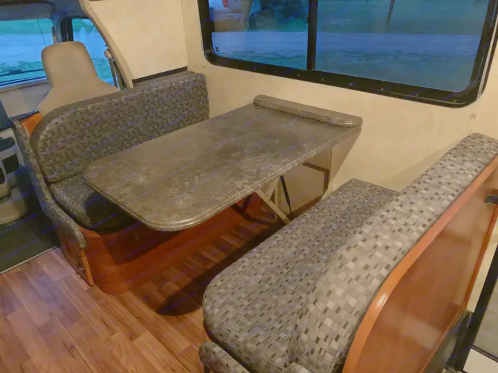 Inside an RV rental: a cozy dinette with a speckled table, patterned benches, and wood flooring for comfortable travel.. Coachmen Freelander 2012