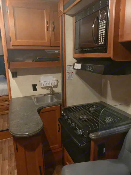 Explore this RV rental's functional kitchen, complete with a microwave, gas stove, sink, and ample wood cabinets.. Coachmen Freelander 2012