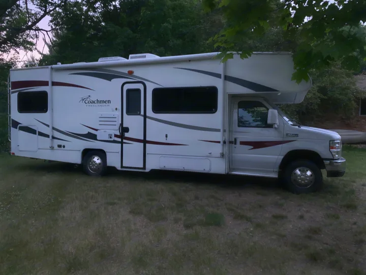 A white Coachmen Freelander Class C RV rental parked on grass, surrounded by trees.. Coachmen Freelander 2012