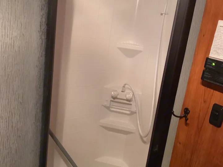 A compact, white shower stall with a handheld showerhead and built-in shelves, typical of an RV rental bathroom.. Coachmen Freelander 2012