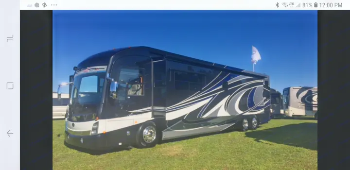 A sleek, black and white luxury motorhome (RV) with blue accents, parked on green grass. Perfect for RV rental adventures.. American Coach 42B 2019