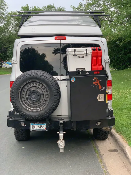 Rear view of a silver RV rental van. Equipped with a raised roof, spare tire, Yeti cooler, and cargo box, ideal for adventure.. Roadtrek N6-Active 2013
