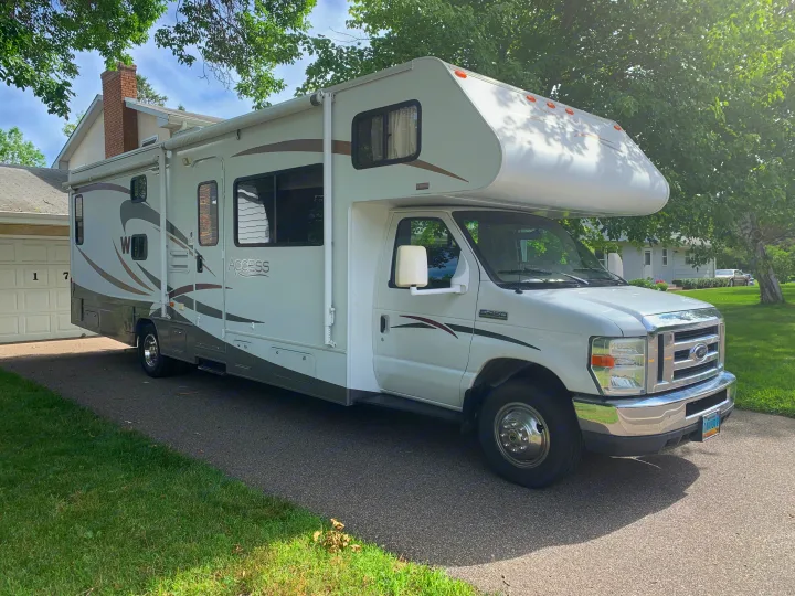 White & grey Class C motorhome RV rental parked on a paved driveway. Sunny day with green trees & grass.. Winnebago Access 2008