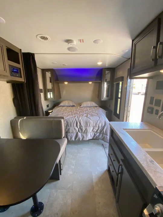 Spacious RV rental interior showing a comfortable bedroom with ambient lights, a functional kitchen, and a cozy dinette.. Jayco Jay Flight 2020