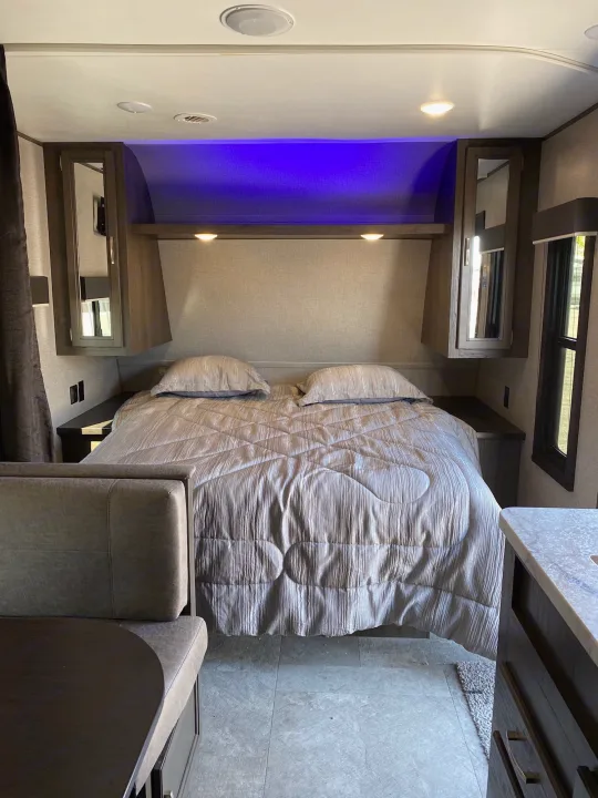 Cozy RV rental interior featuring a modern bedroom with a gray comforter, blue ambient lighting, and a dinette area.. Jayco Jay Flight 2020