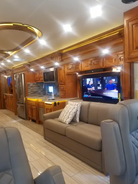Spacious luxury RV rental interior features a modern kitchen, living area with sofa, large TV, and elegant wood cabinetry.. American Coach 42B 2019