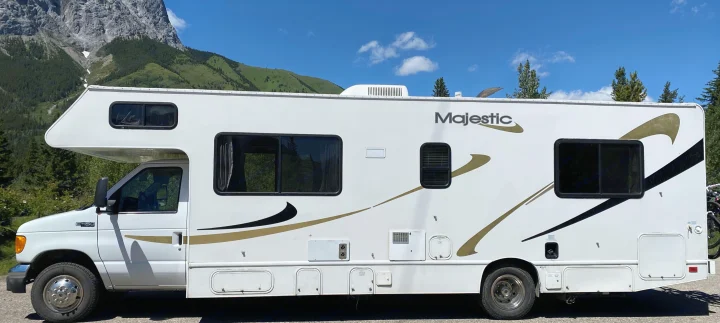 White Majestic **RV rental** parked against a backdrop of green mountains and a blue sky, ready for outdoor adventure.. Ford Cutaway 2006
