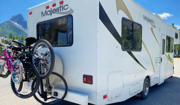 White Majestic rv rental with bikes on the back, parked in a scenic mountain setting under a blue sky, ready for adventure.. Ford Cutaway 2006