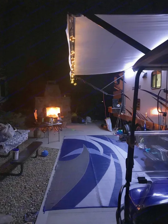 Cozy night at an RV rental site: Family by a fireplace, under a lighted awning, with an outdoor mat.. Other Other 2018