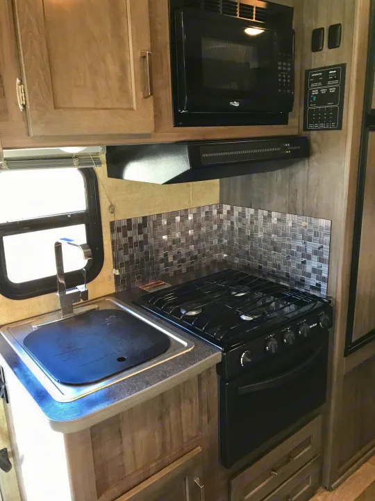 This RV rental kitchen features a compact sink, oven/stove, microwave, and integrated control panel.. Winnebago Minnie Winnie 2019