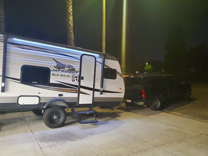 Night view: A white Jayco Jay Flight SLX Baja travel trailer (RV rental), with its awning light on, hitched to a black SUV.. Jayco Jay Flight 2019