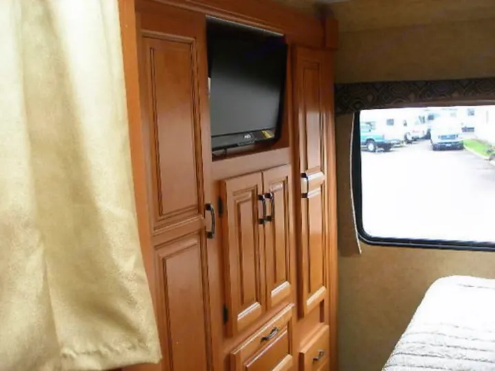 Inside a cozy RV rental: wooden bedroom cabinetry with TV, and a window view, offering comfort for your travels.. Forest River Sunseeker LE 2015