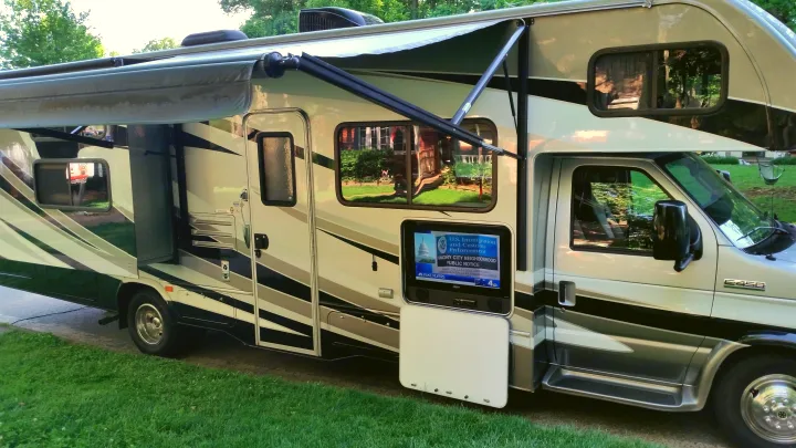 An RV rental is parked with an extended awning and an outdoor TV displaying a U.S. Immigration and Customs Enforcement public notice.. Forest River Sunseeker LE 2015