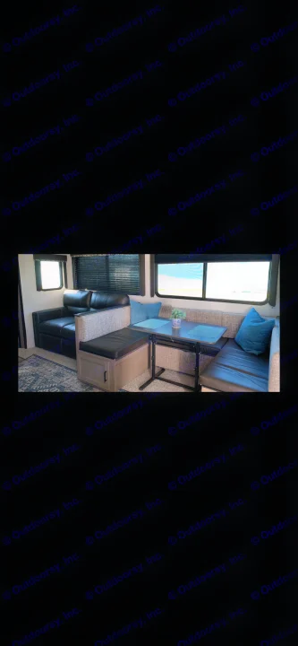 Spacious RV rental interior featuring a comfortable black sofa and a versatile dinette with blue accents and a table.. Keystone Bunkhouse 2020