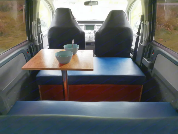 Compact RV rental interior with a wooden table, bowls, and blue cushioned seating/beds, designed for cozy travel.. honda stepwagon 2006