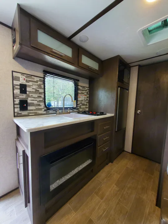 RV rental kitchen: modern counter, sink, cooktop, microwave, fridge, tile backsplash, and electric fireplace.. Dutchmen Coleman 2021