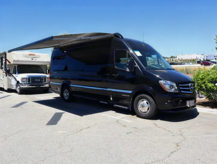 Black Airstream Sprinter van with awning extended, next to white Class C RV, both ideal for rv rental adventures.. Airstream Interstate 2019