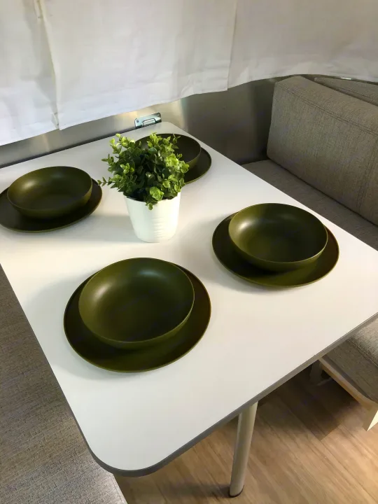 Cozy RV rental dinette setup with olive green dishware and a plant. Perfect for meals on the go in your travel trailer.. Airstream Bambi 2021