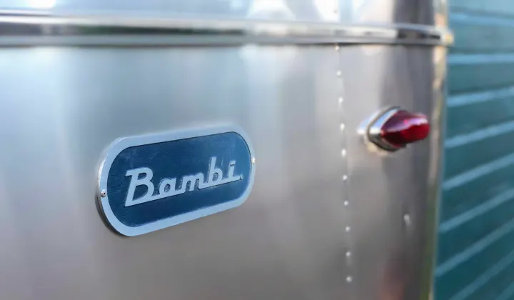 Close-up of a vintage silver Airstream Bambi RV rental. Its classic nameplate and red taillight gleam on the polished exterior.. Airstream Bambi 2021