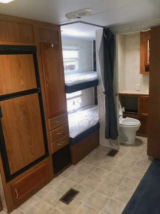 RV rental interior with bunk beds, a compact bathroom, and kitchen area featuring a refrigerator and wood cabinets.. Forest River Wildwood 2005