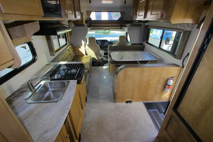 Spacious rv rental interior featuring a kitchen with sink and stove, a dinette booth, and the driver's cabin up front.. Coachmen Leprechaun 2020