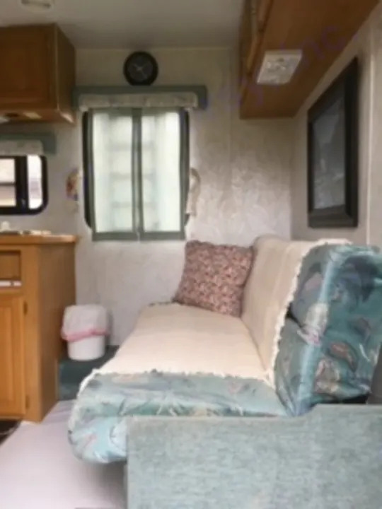 This **RV rental** features a cozy **living area** with a patterned **couch**, window, and warm wood cabinets, ready for travel.. Electra Electra 1996