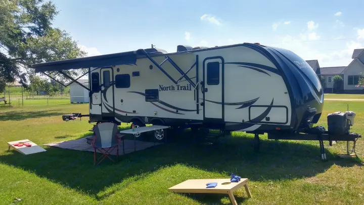 Enjoying an RV rental: a North Trail travel trailer with an extended awning, ready for outdoor fun with cornhole!. Heartland North Trail 2015