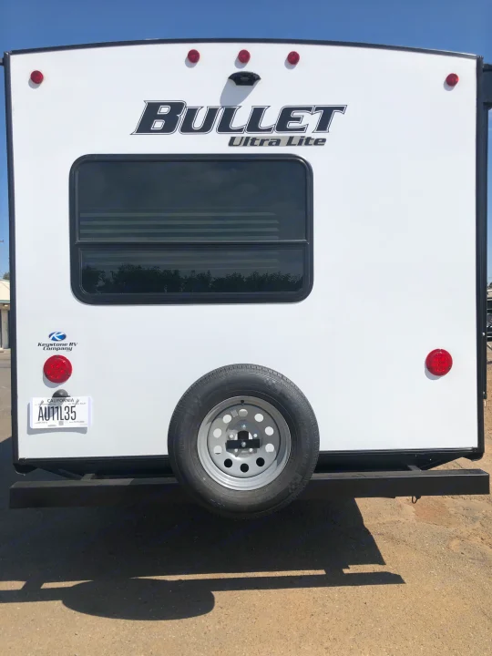 White Bullet Ultra Lite RV rental rear view, with California plate AU11L35, window, and spare tire for travel.. Keystone Bullet 2021