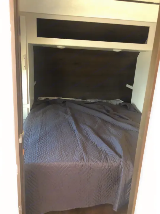 Cozy RV rental sleeping area featuring a quilted grey bed and white built-in storage cabinets.. Keystone Bullet 2021
