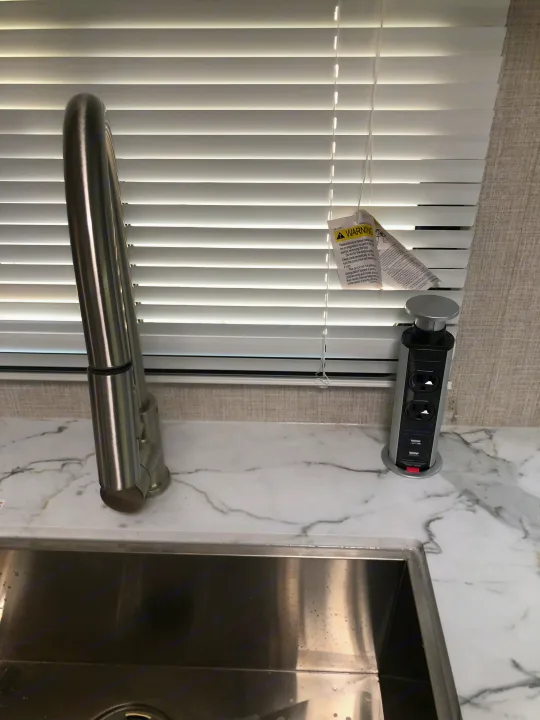 RV rental kitchen: Stainless sink, faucet, pop-up outlet, and blinds with a warning tag.. Keystone Bullet 2021