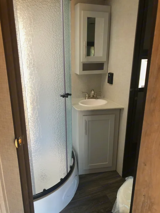 Inside an RV rental, a clean bathroom with a modern vanity, sink, mirrored medicine cabinet, and a curved glass shower.. Keystone Bullet 2021
