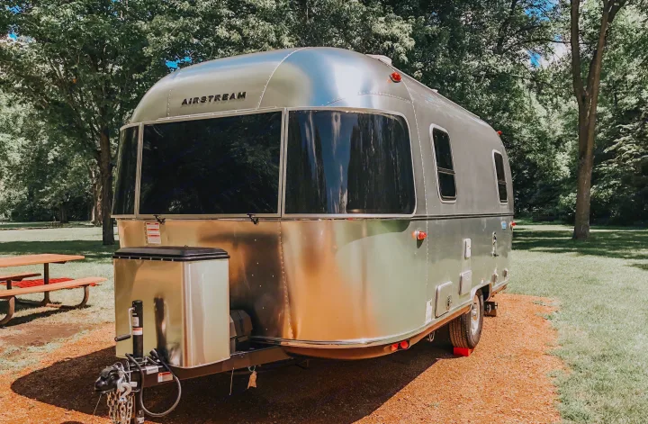 This gleaming Airstream travel trailer, ready for an rv rental, sits parked in a sunny, green campground.. Airstream Bambi 2021